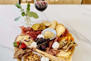 A small charcuterie board with meats, cheese, fruit, and breads paired with red wine, sitting on white granite countertop inside Adelphos Cellars' tasting room